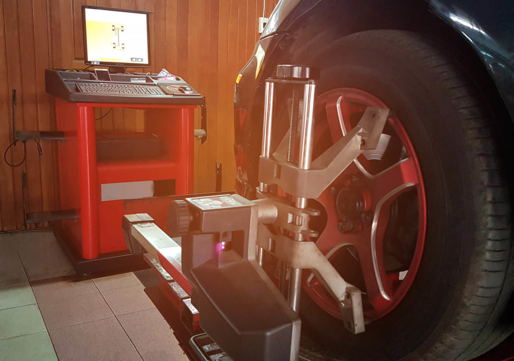 The black car prepairing for wheel alignment or balancing tire wheel machine at tyre service center, as background automotive concept.